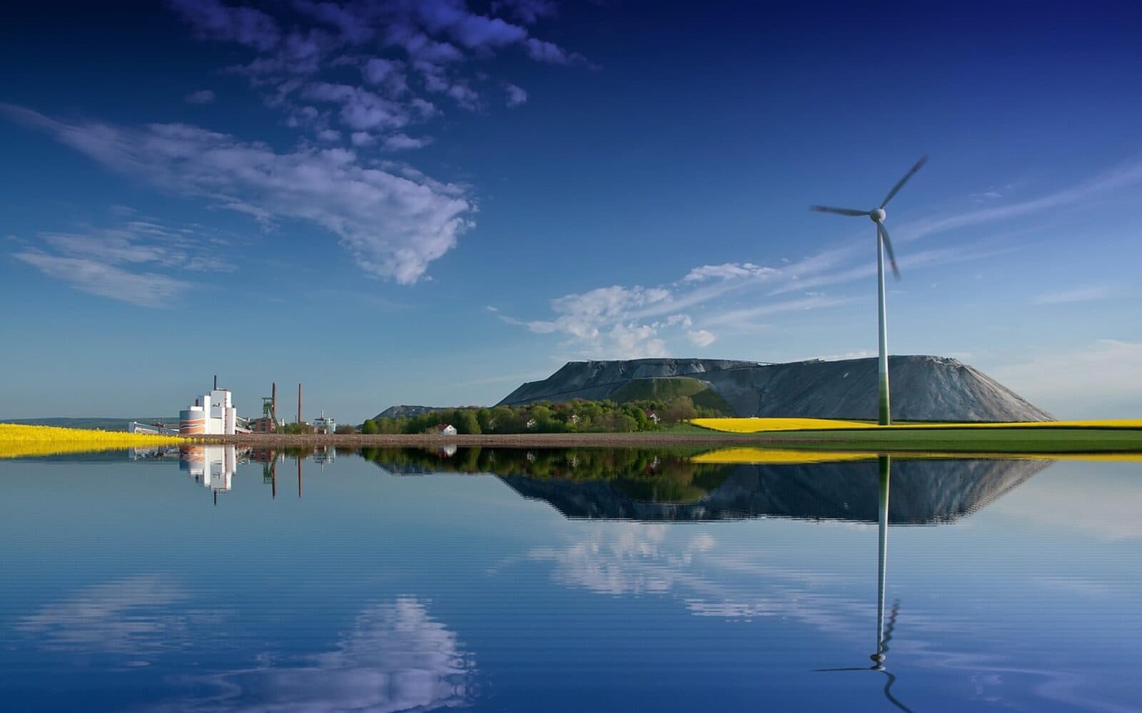 Concept image of a rehabilitated MSC Mining site next to a wind turbine, fields and a calm reflective water body under a blue sky.