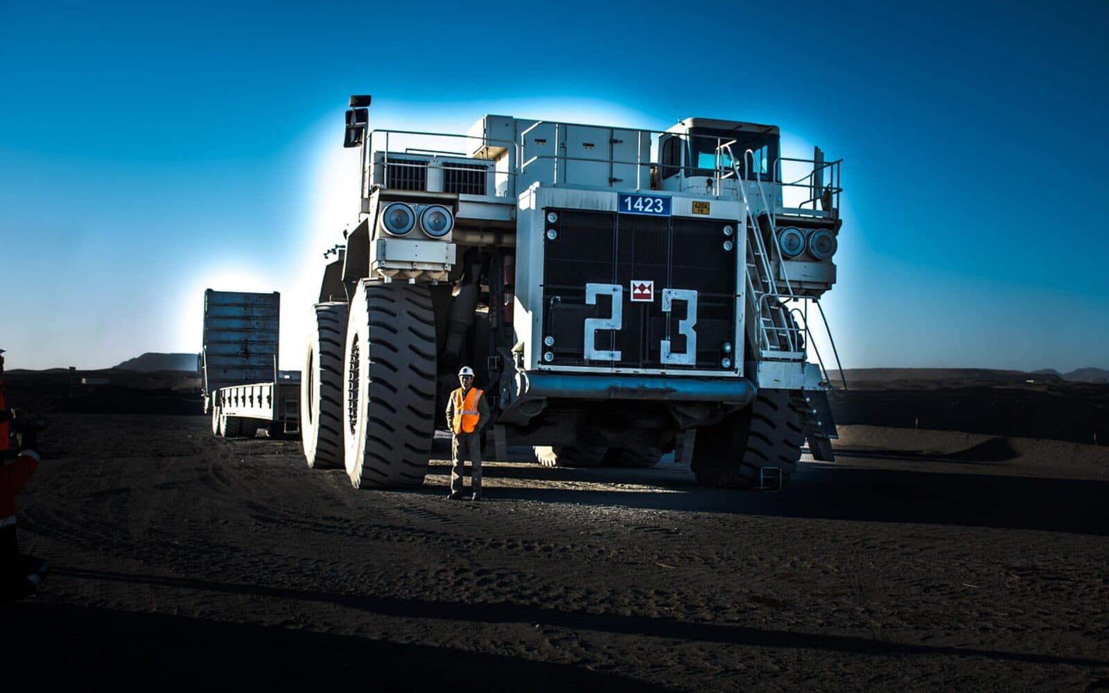 Concept image of an MSC Mining worker in a high-visibility safety vest standing in front of a large haul truck on site at sunrise.